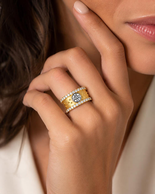 A close-up of a person's hand wearing a gold ring with a large diamond in the center.