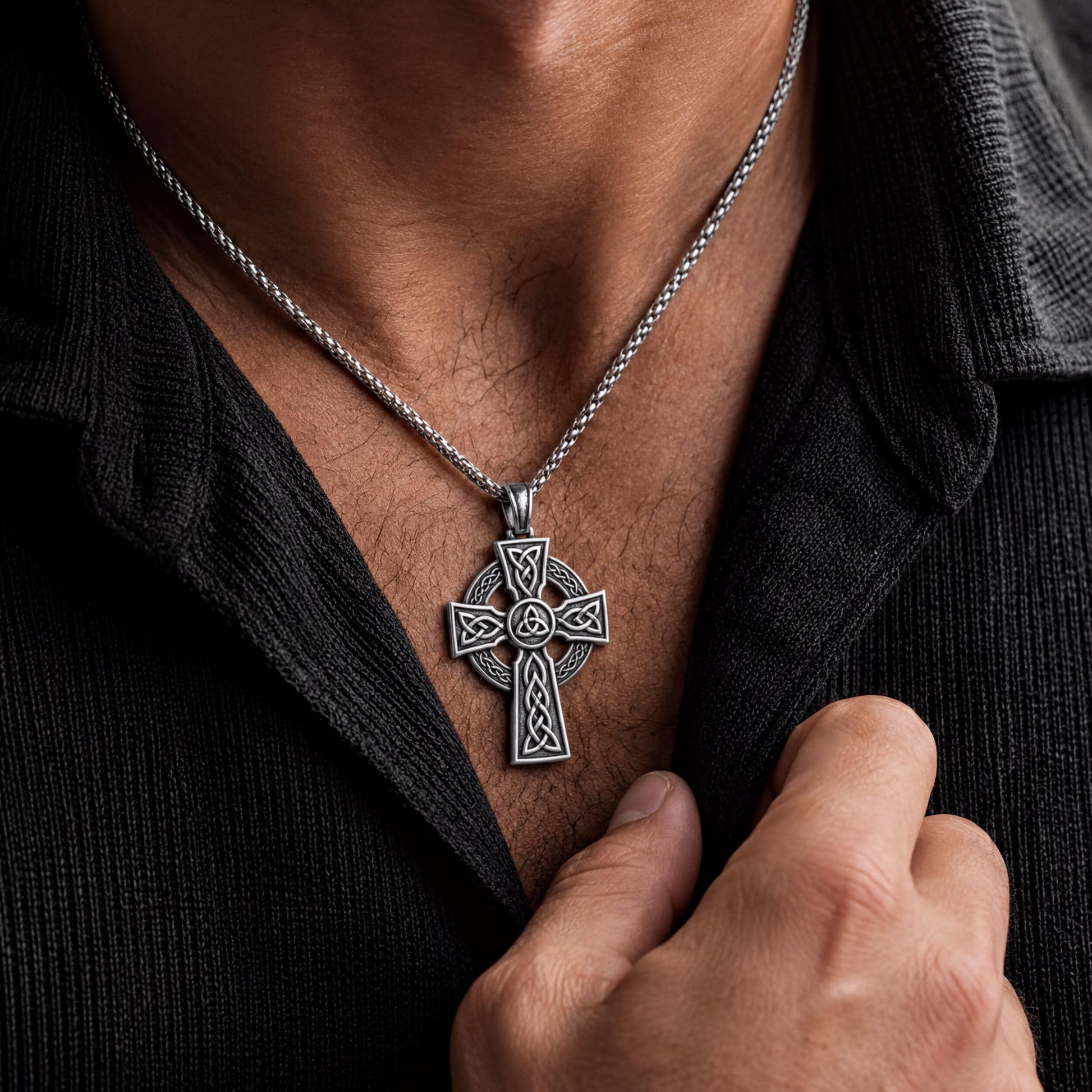A silver cross pendant necklace is worn around a person's neck.