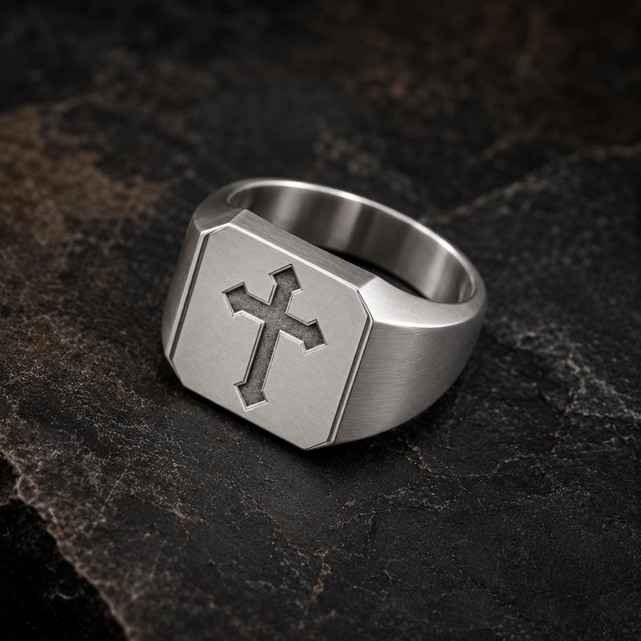 A silver ring with a cross symbol on it, resting on a dark surface.