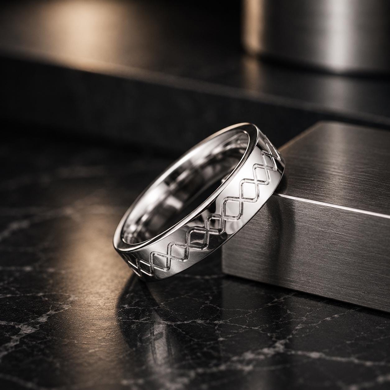 A silver ring with a diamond pattern rests on a black marble surface.