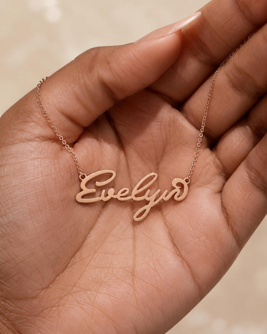 A hand holding a necklace with the name "Evelyn" engraved on it.