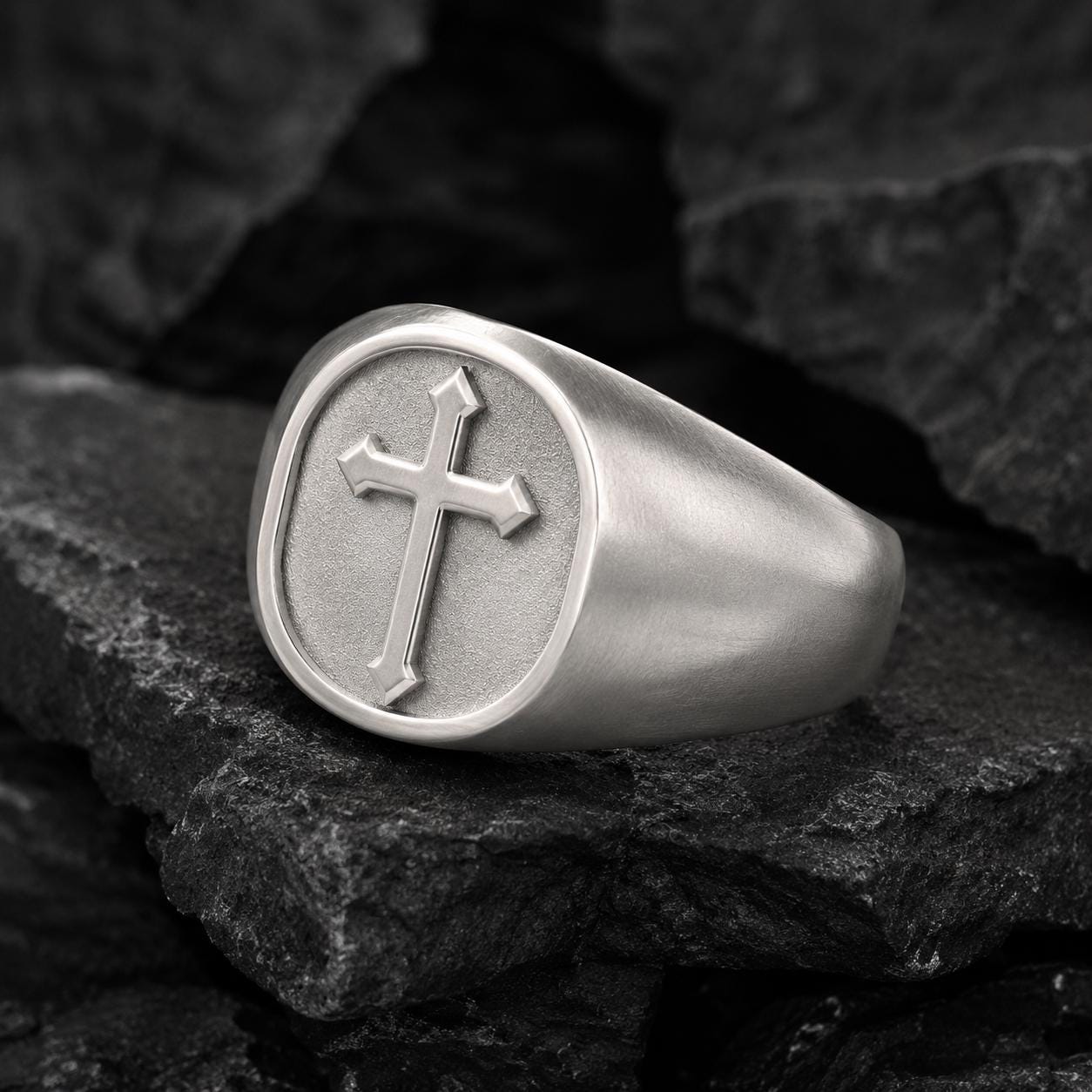 A silver ring with a cross symbol on it, resting on a dark surface.