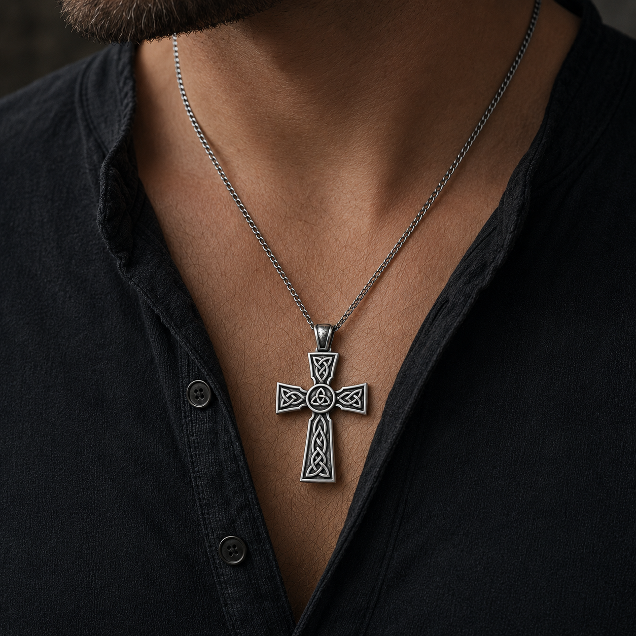 A silver cross pendant necklace is worn by a person in a black shirt.