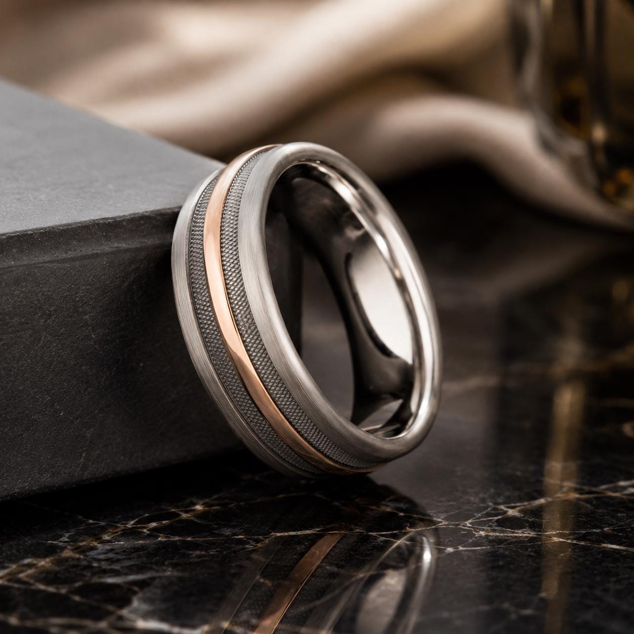 A silver ring with a metallic band and a metallic stripe is resting on a black marble surface.