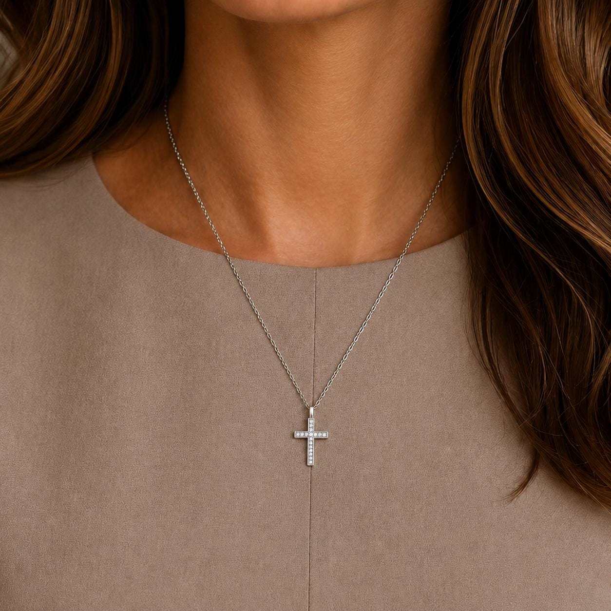 A close-up view of a woman's neck and chest area, showing a silver cross pendant necklace with a diamond accent.