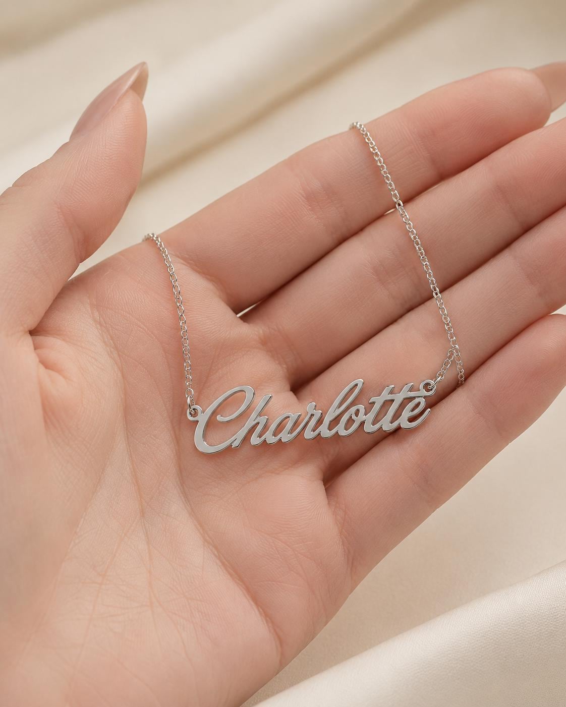 A person's hand holding a necklace with the name "Charlotte" engraved on it.