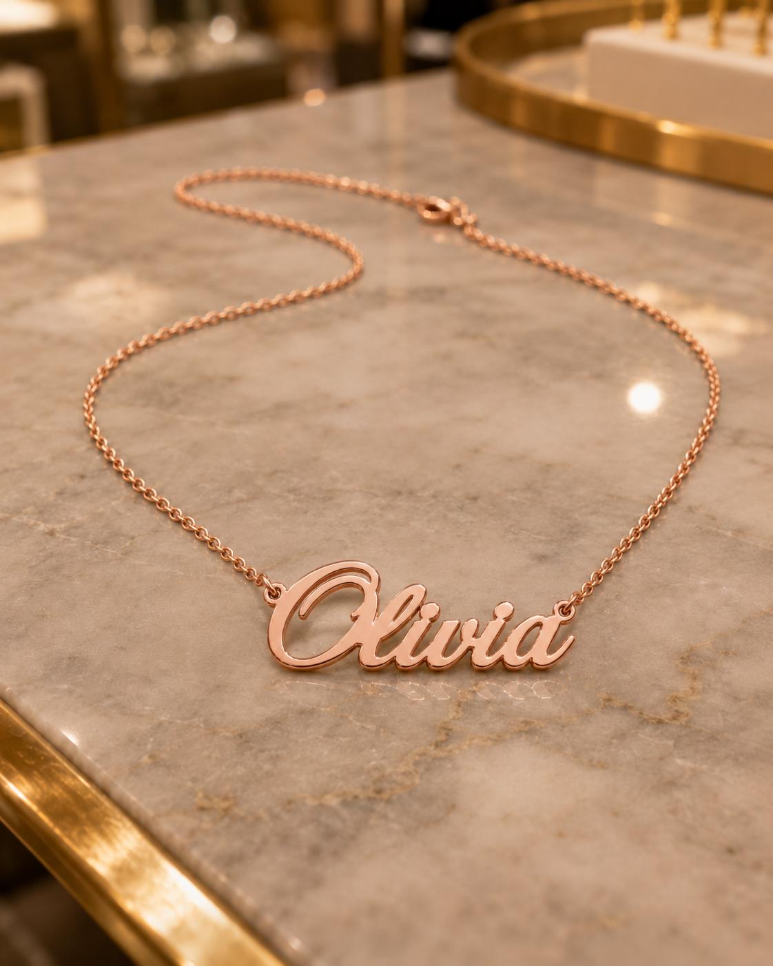 A necklace with the name "Olivia" engraved on it, resting on a marble surface.