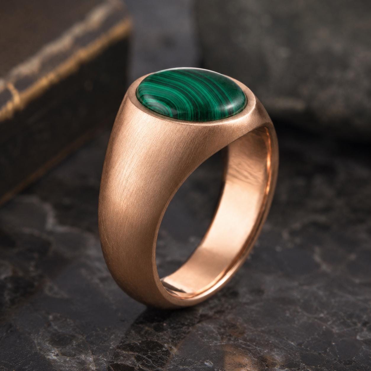 A gold ring with a large oval-shaped green gemstone, likely malachite, set in the center of the band.