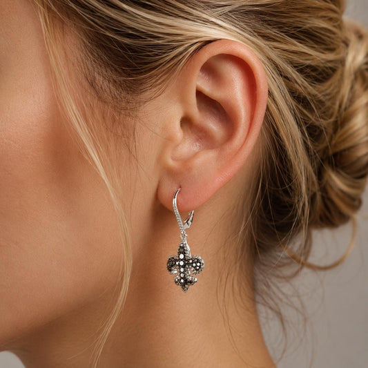 A close-up of a woman's ear wearing a pair of silver earrings with a floral design.