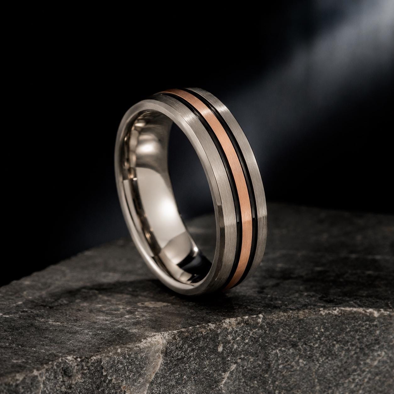 A silver ring with a metallic band featuring a horizontal stripe of copper-colored material, resting on a dark surface.