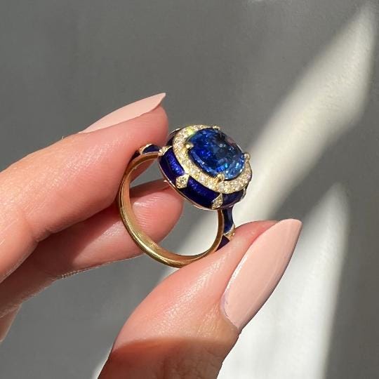 A hand holding a gold ring with a blue gemstone, which appears to be a sapphire.