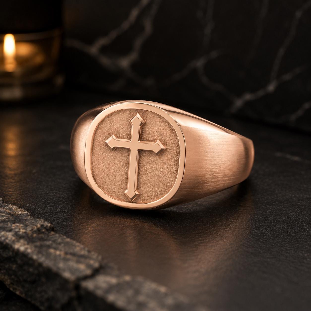 A gold-colored signet ring with a cross design on the front, placed on a dark surface.