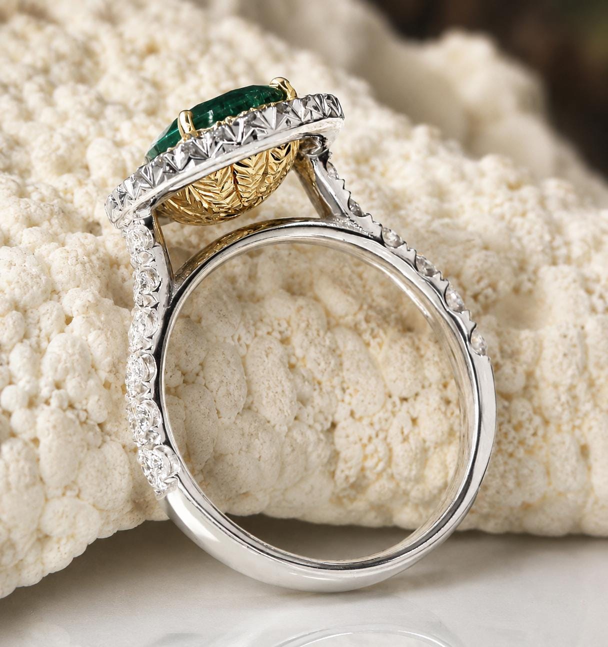 A silver ring with a large green gemstone, likely an emerald, set in a halo of smaller diamonds.