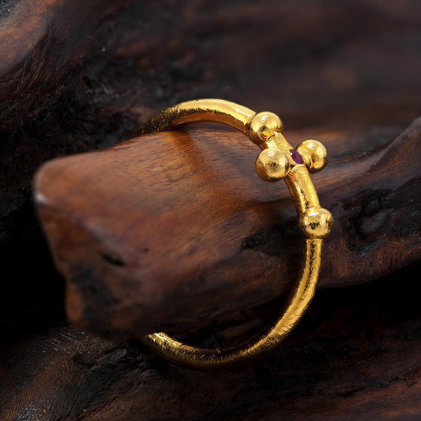 A gold ring with a unique design rests on a wooden surface.