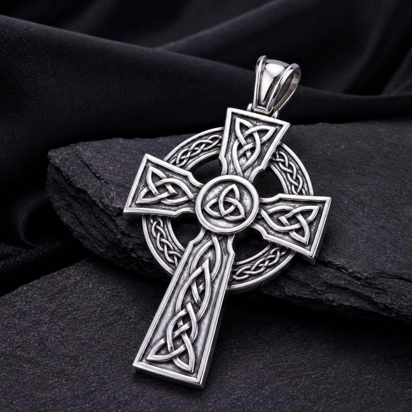 A silver-colored Celtic cross pendant with intricate designs and patterns, resting on a dark surface.