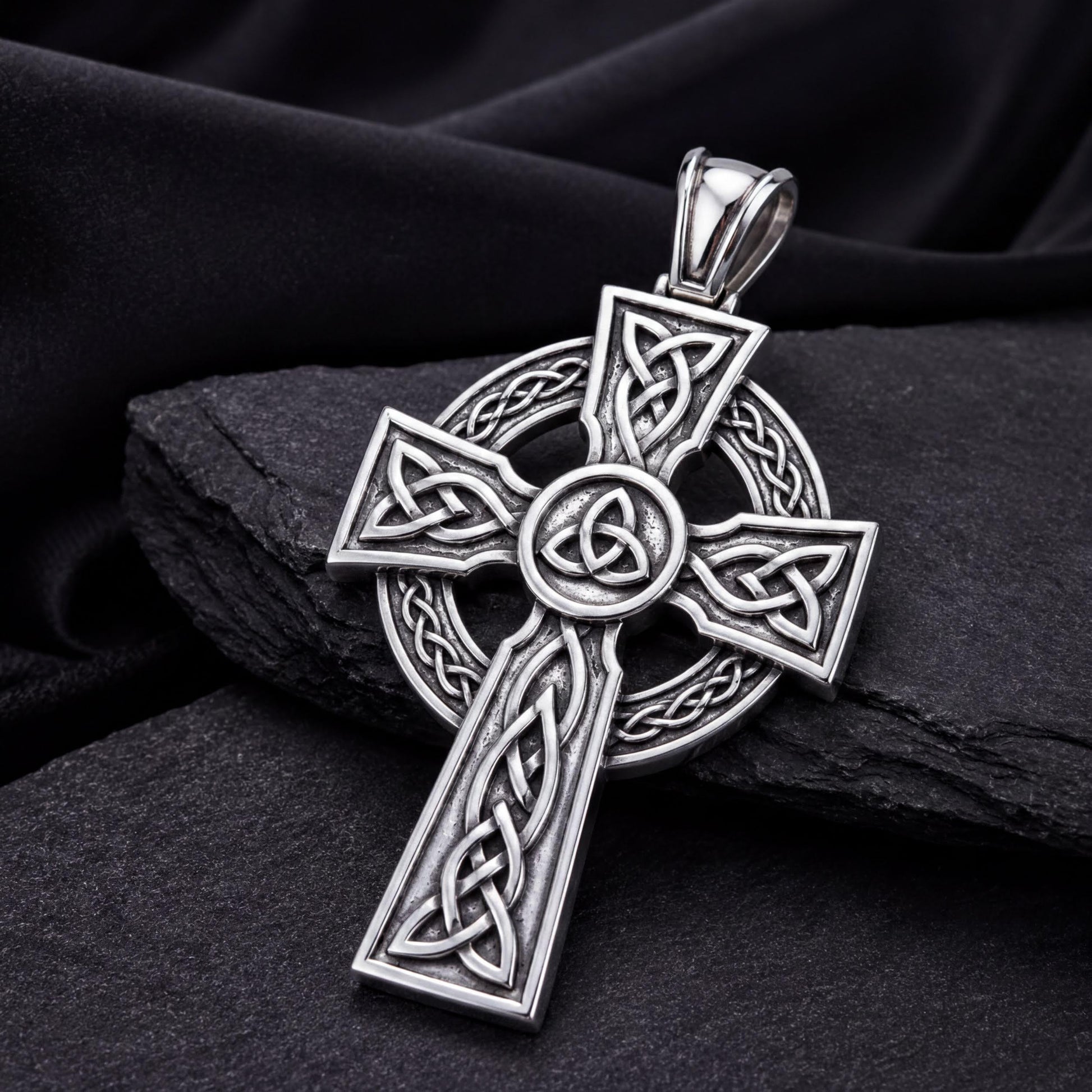 A silver-colored Celtic cross pendant with intricate designs and patterns, resting on a dark surface.