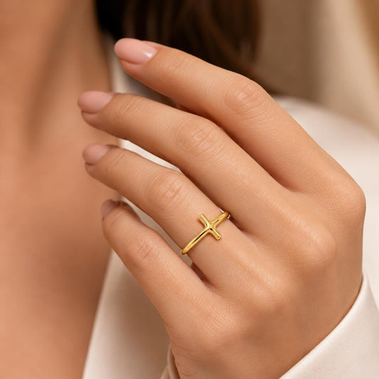 A close-up of a person's hand wearing a gold cross ring on the ring finger.