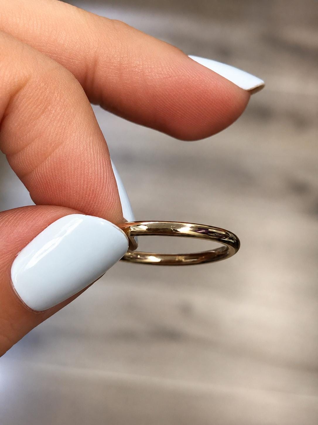 A close-up view of a person's fingers holding a gold ring against a blurred background.
