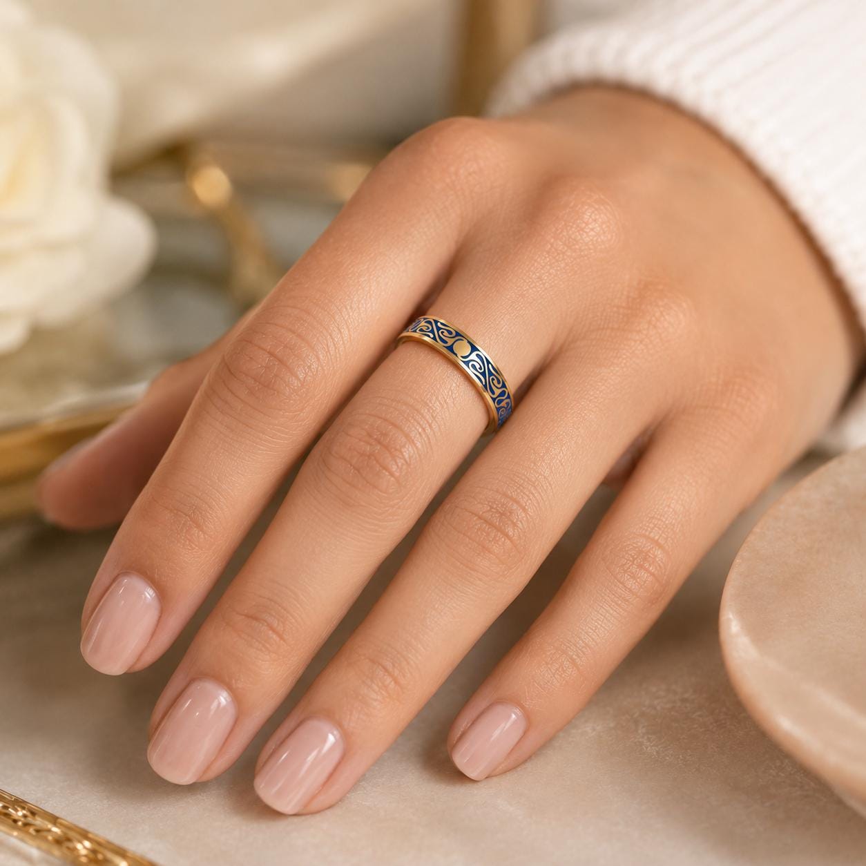 A close-up of a hand wearing a gold ring with blue and gold designs.
