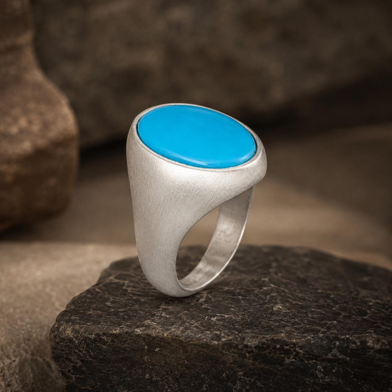 A silver ring with a blue stone sits on a rock.