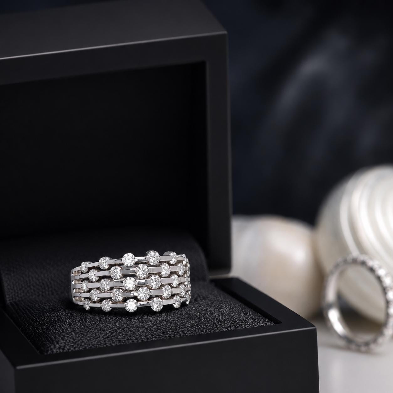 A diamond ring is displayed in a black jewelry box, with a blurred background of other jewelry pieces.