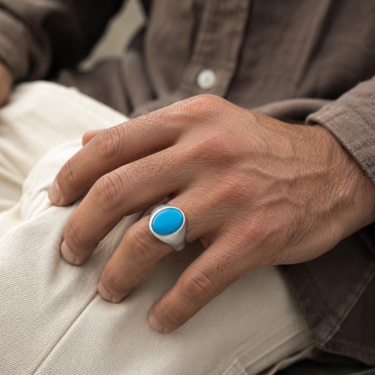 A close-up image of a person's hand wearing a silver ring with a blue oval stone.