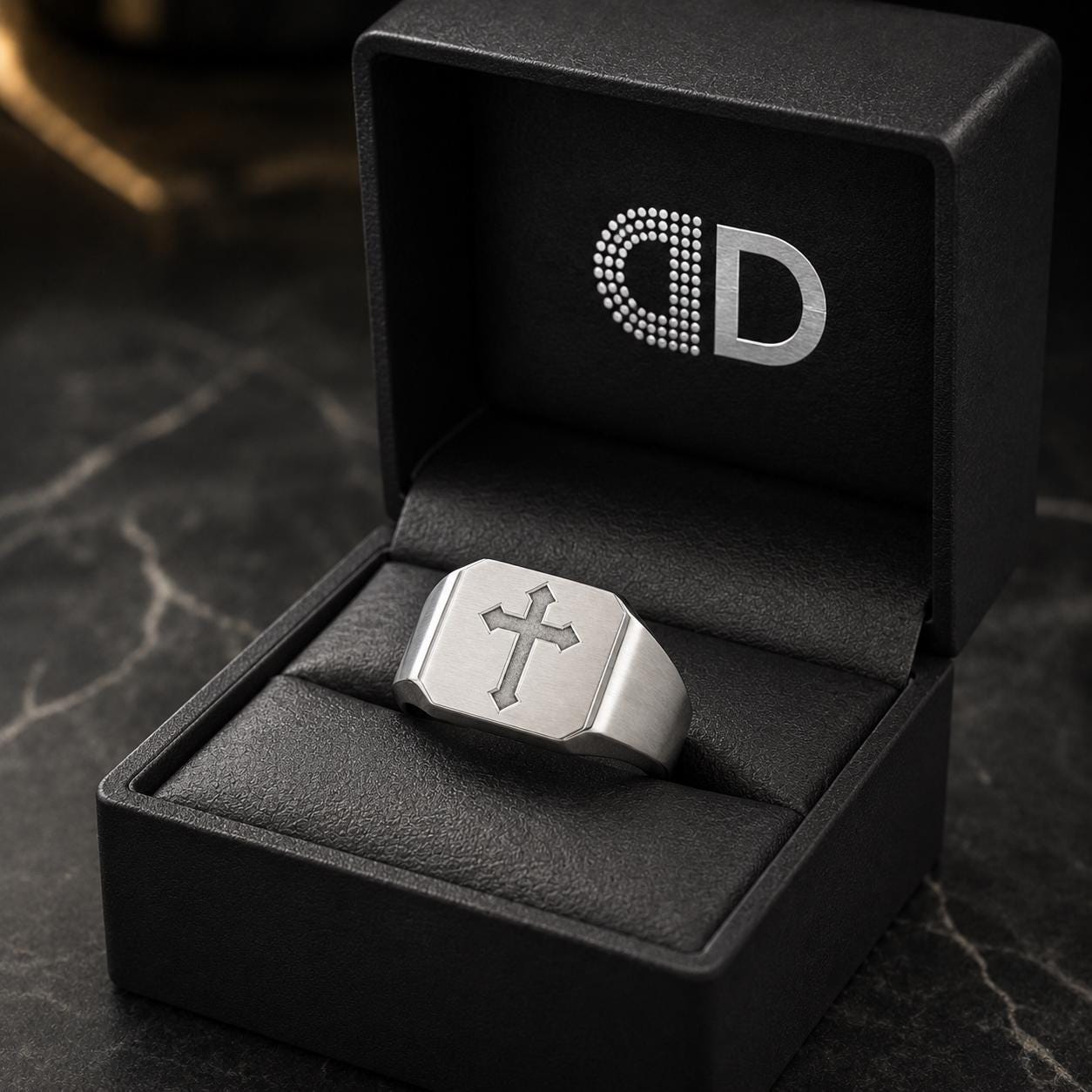 A silver ring is displayed in a black jewelry box with a logo on the lid.