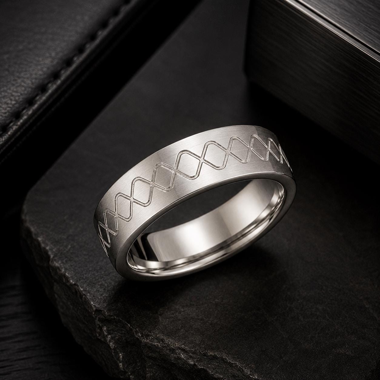A silver ring with a unique design sits on a black surface.