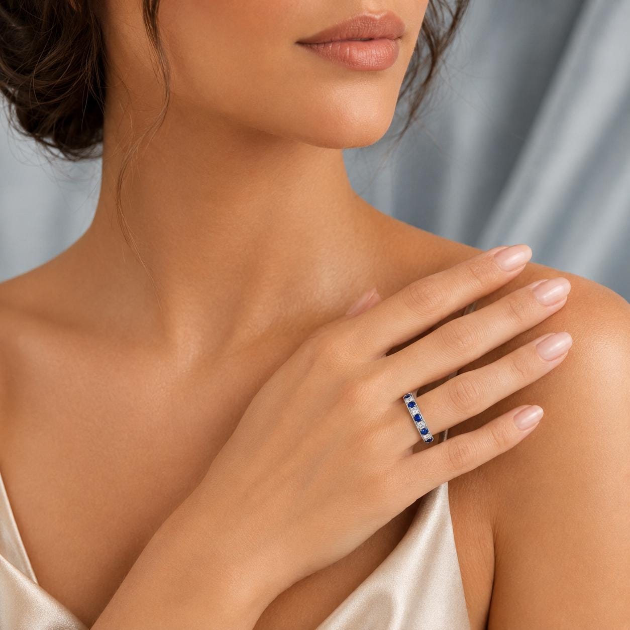 A close-up of a woman's hand wearing a ring with blue stones, resting on her shoulder.