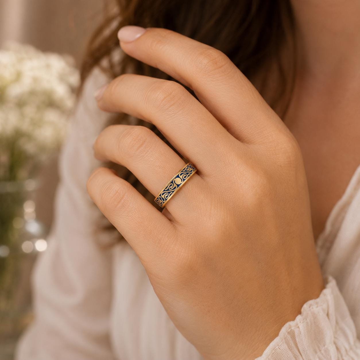 A close-up of a person's hand wearing a gold ring with a decorative design.