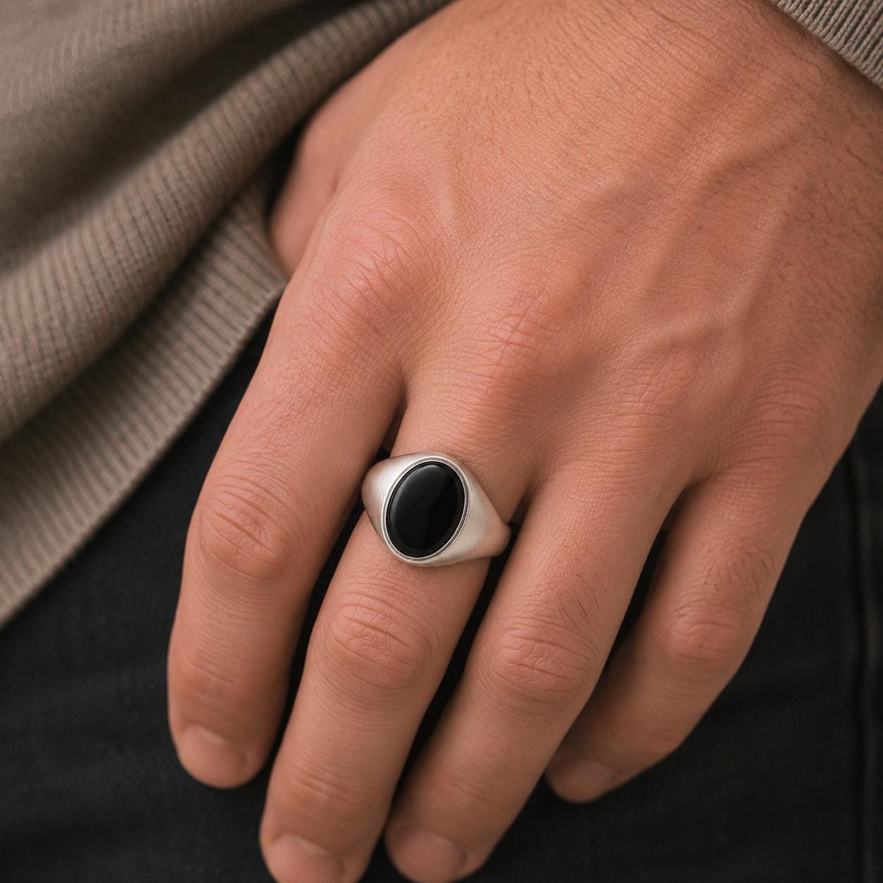 A close-up of a person's hand wearing a silver ring with a black oval stone.