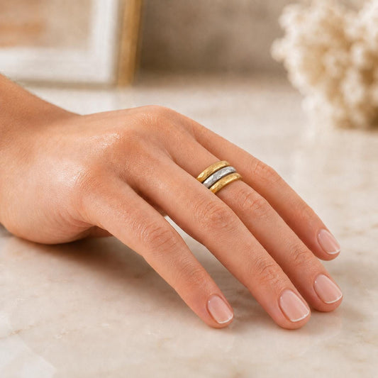 A close-up of a hand wearing a ring on the ring finger, resting on a marble surface.