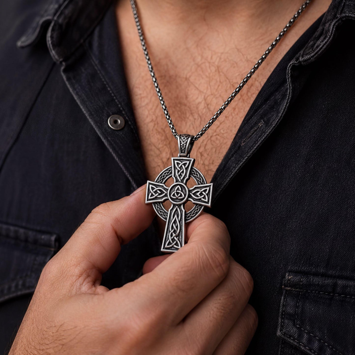 A person wearing a silver cross necklace is holding the cross pendant up to their neck.