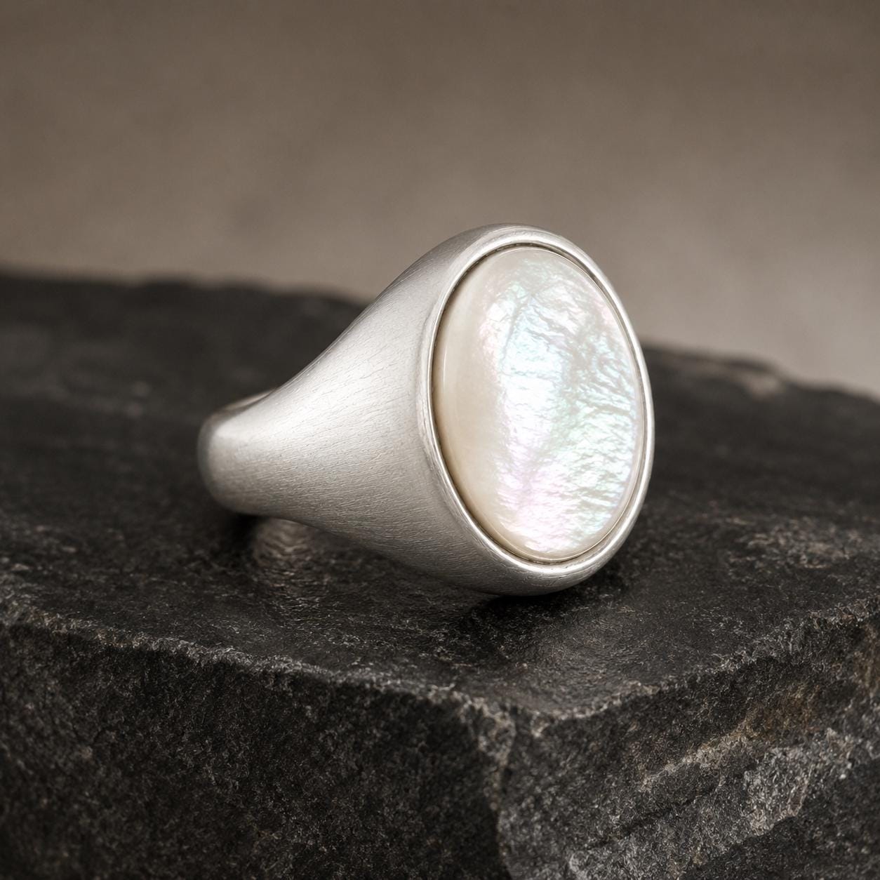 A silver ring with a large oval-shaped pearl sits on a dark gray rock.