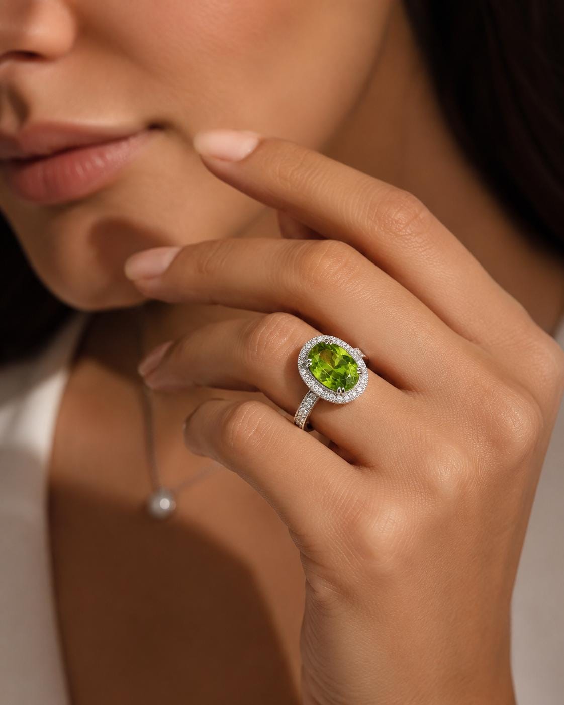 A close-up of a person's hand wearing a large, oval-shaped ring with a green gemstone, likely an emerald, set in a halo of smaller diamonds.