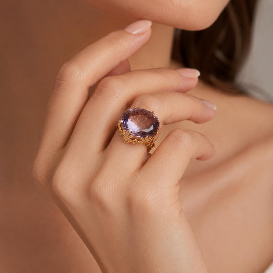 A close-up of a person's hand wearing a large, ornate ring with a purple gemstone.
