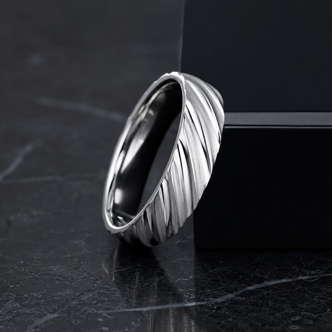 A silver ring with a unique, textured design rests on a dark surface, creating a striking contrast.