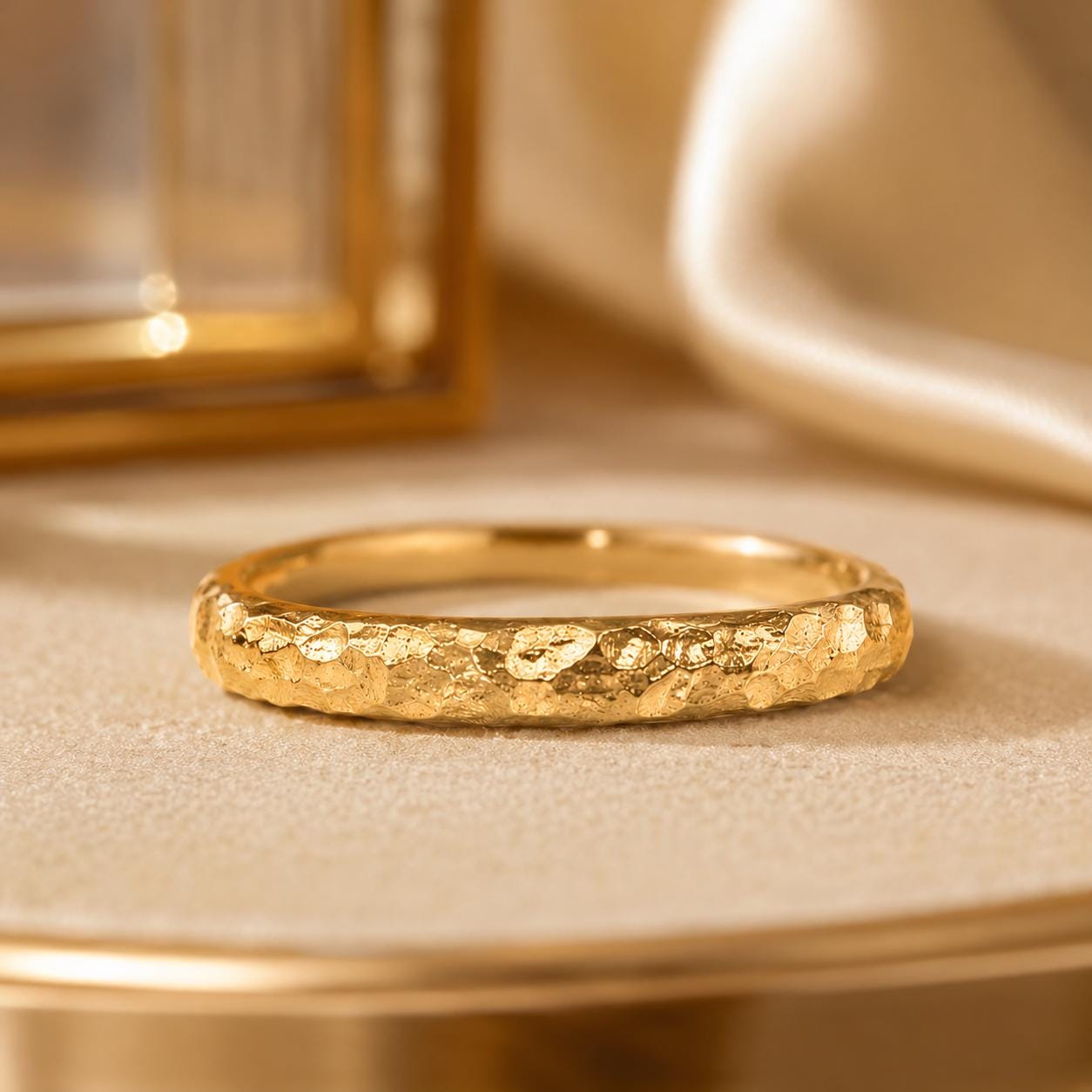 A close-up image of a gold ring with a textured surface, placed on a beige surface.
