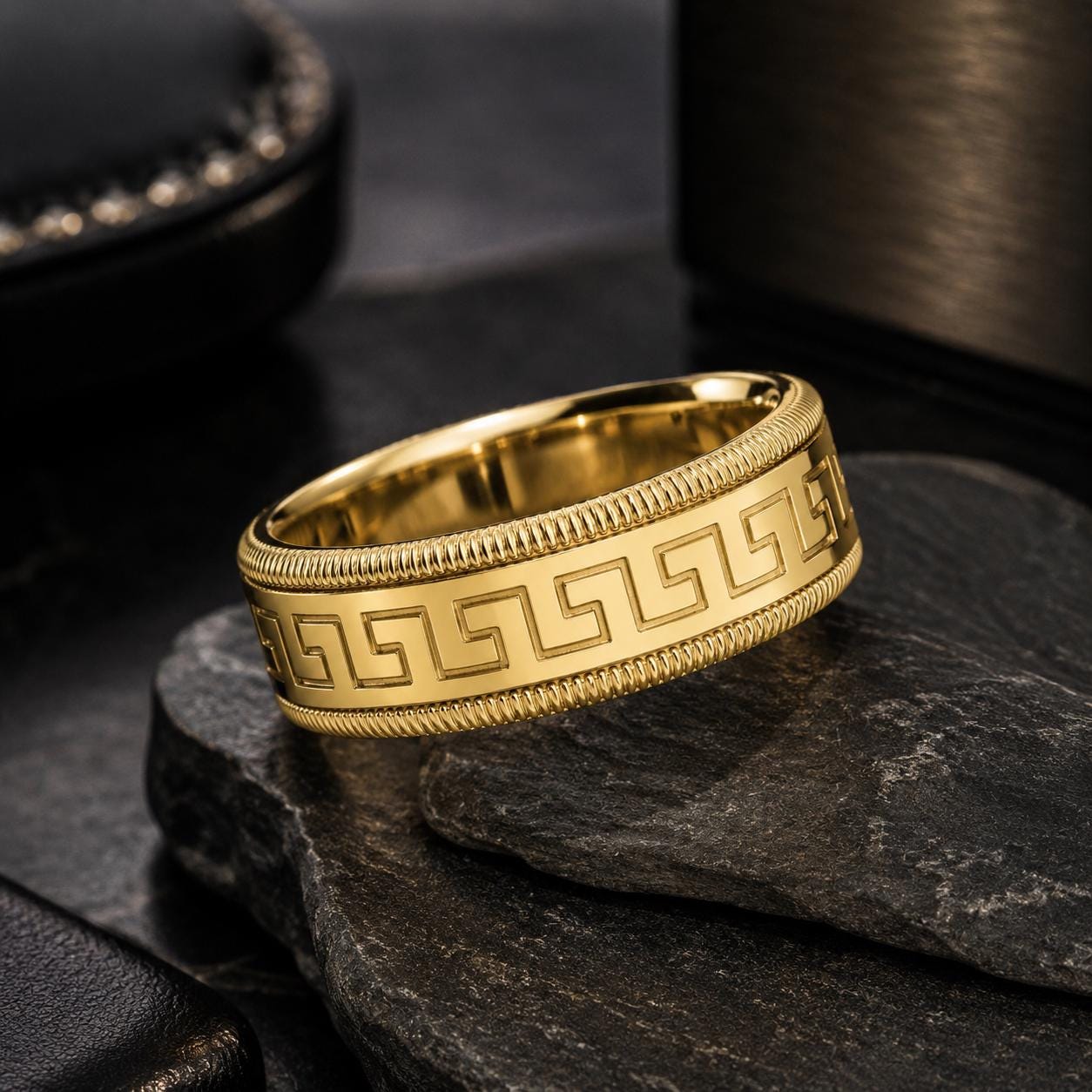 A gold ring with a Greek key pattern is displayed on a black surface.