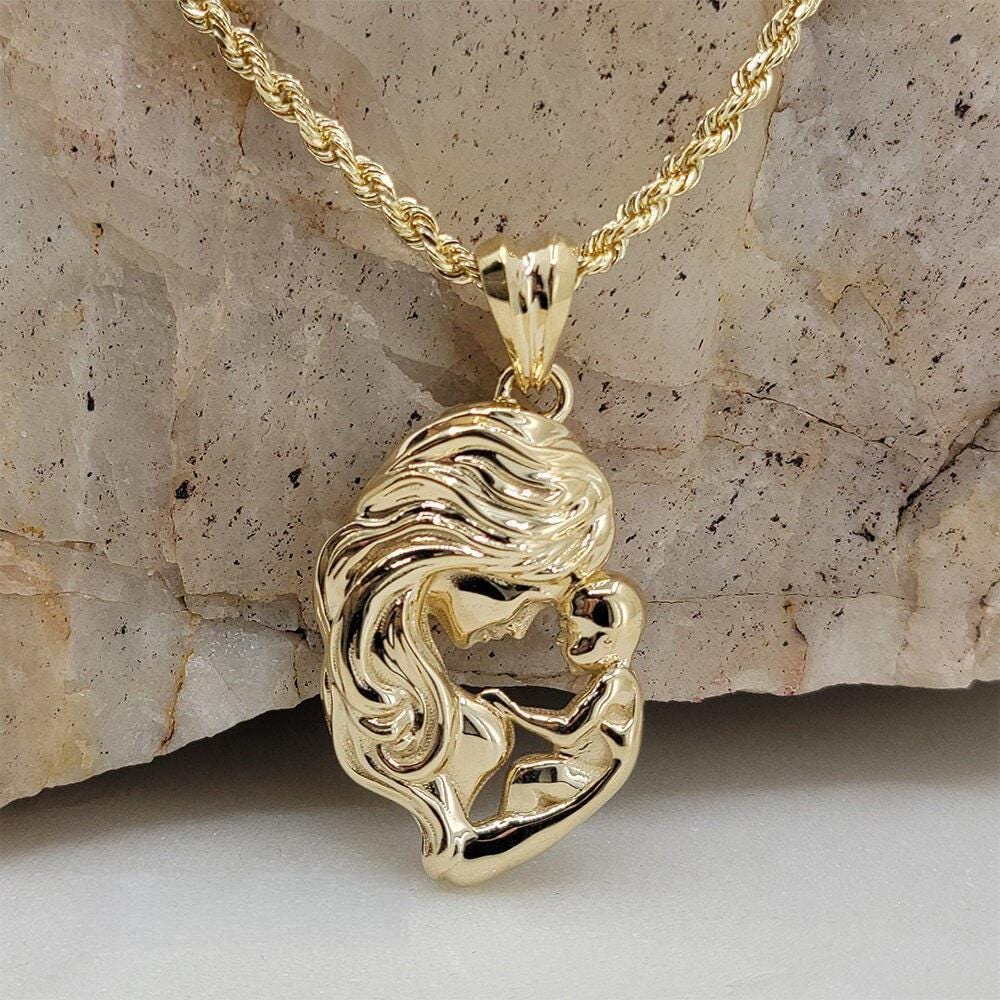 A gold-colored pendant necklace with a pendant in the shape of a woman's face, possibly a mother and child, is displayed against a stone background.