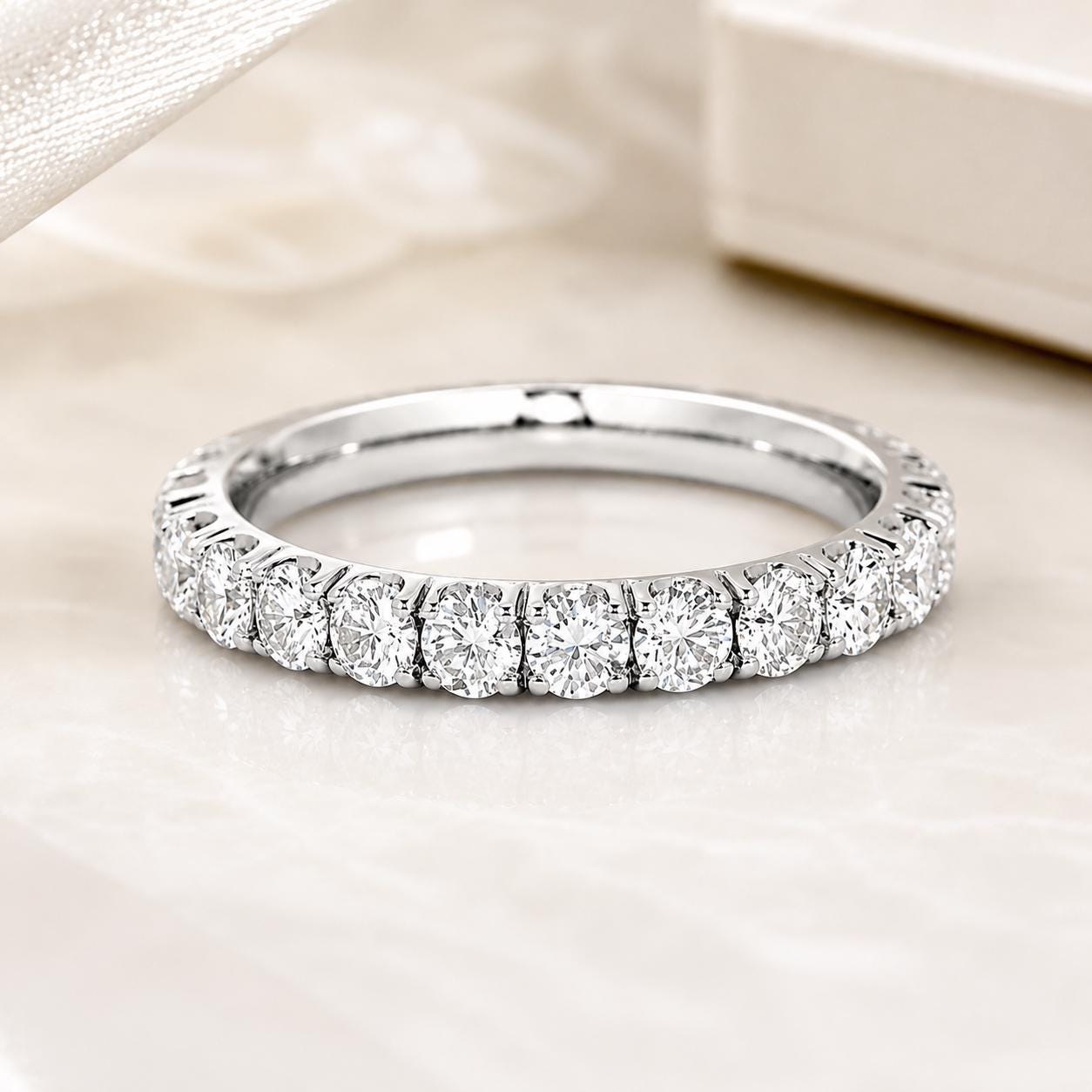 A diamond ring with a row of round diamonds set in a silver band, resting on a white surface.