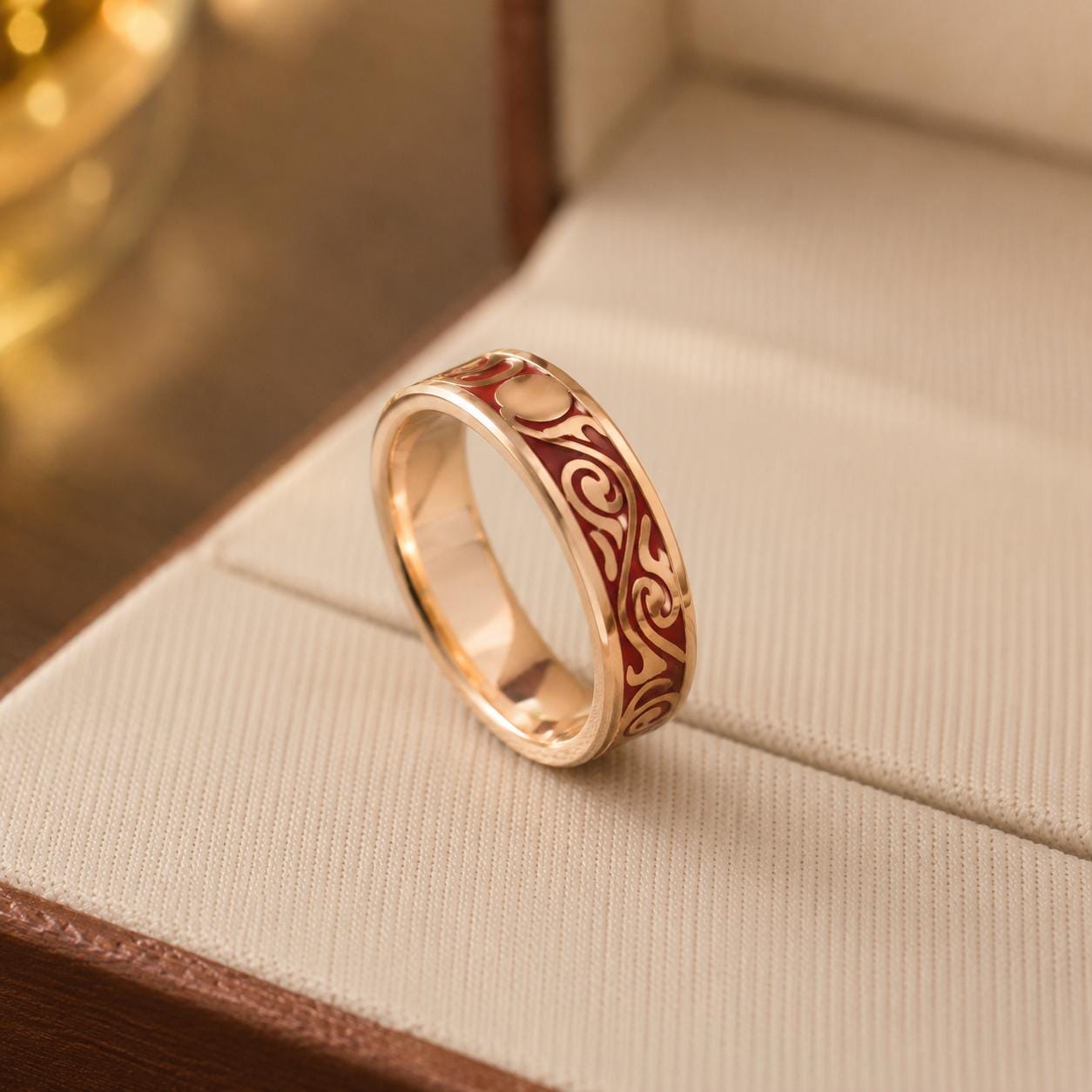 A gold ring with a red and gold design sits on a white fabric surface.