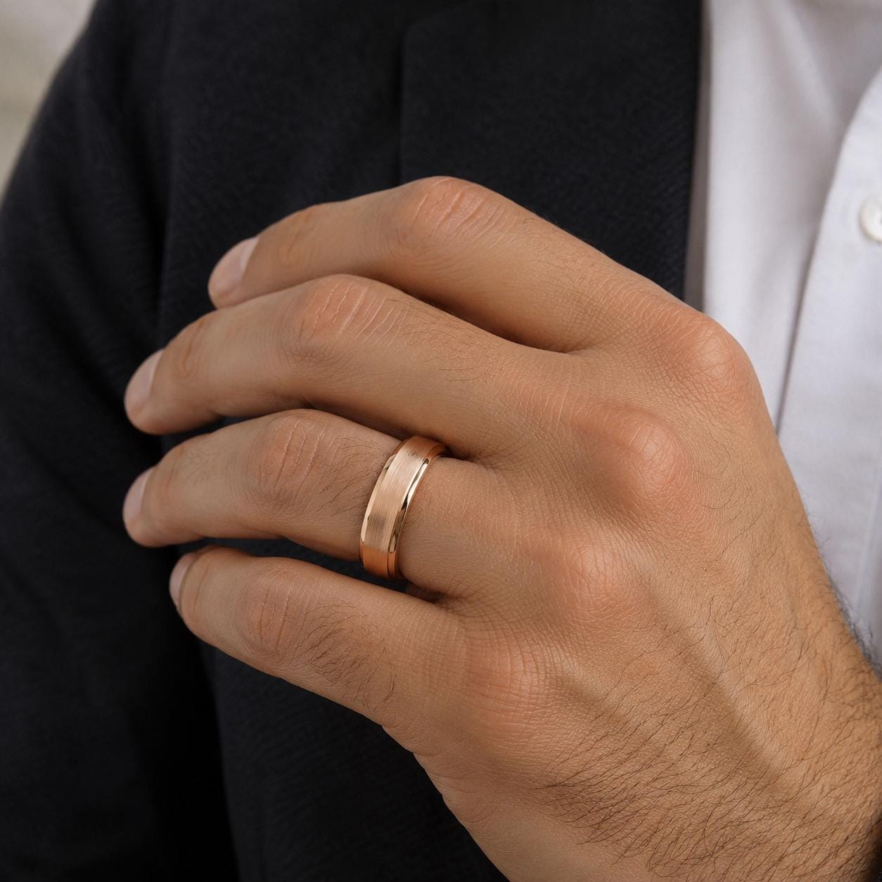 A close-up of a person's hand wearing a gold ring, with a black jacket visible in the background.
