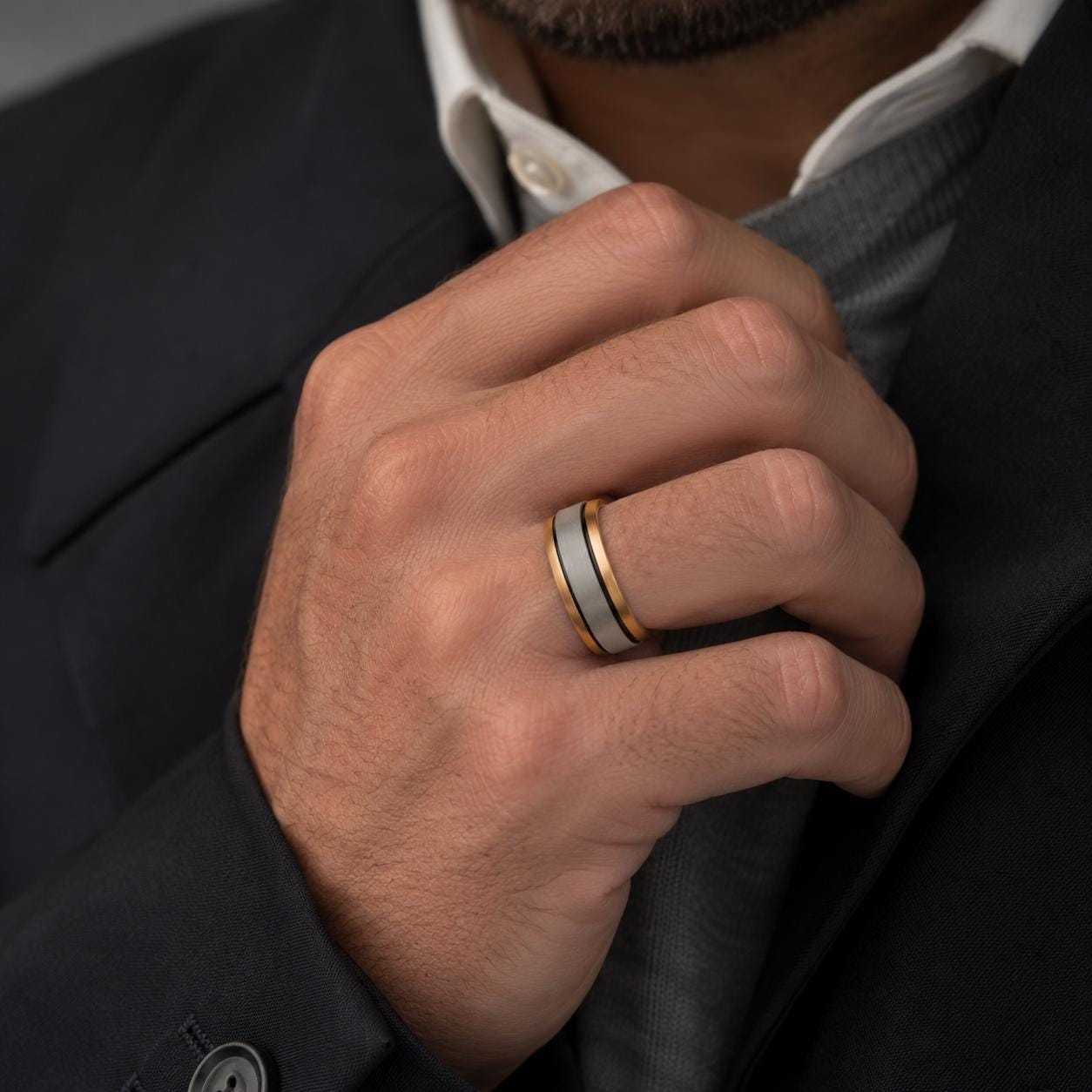A close-up of a man's hand wearing a ring, with a suit jacket visible in the background.