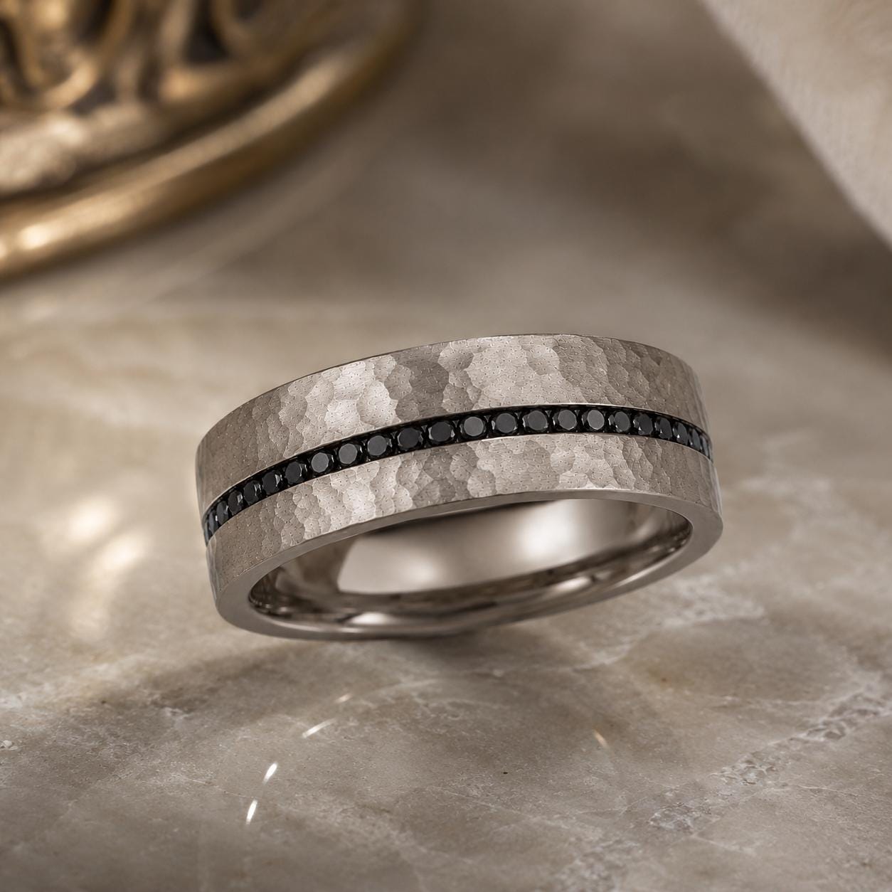 A silver ring with a horizontal band of black diamonds is displayed on a marble surface.