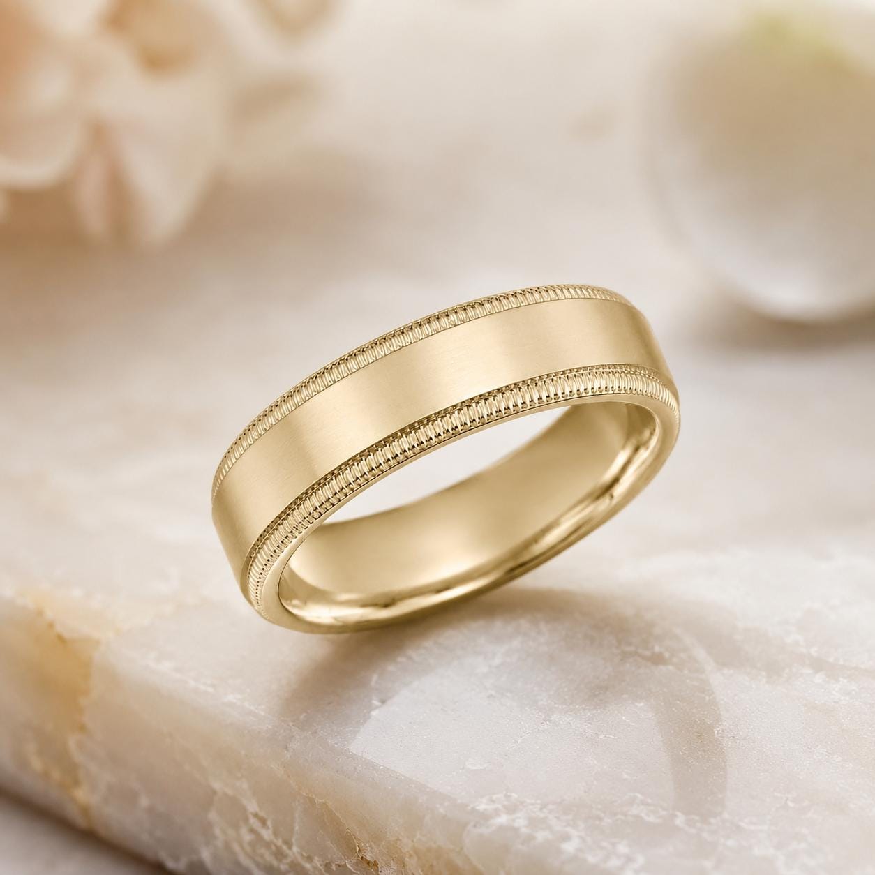 A gold wedding band with a smooth, polished finish sits on a marble surface.