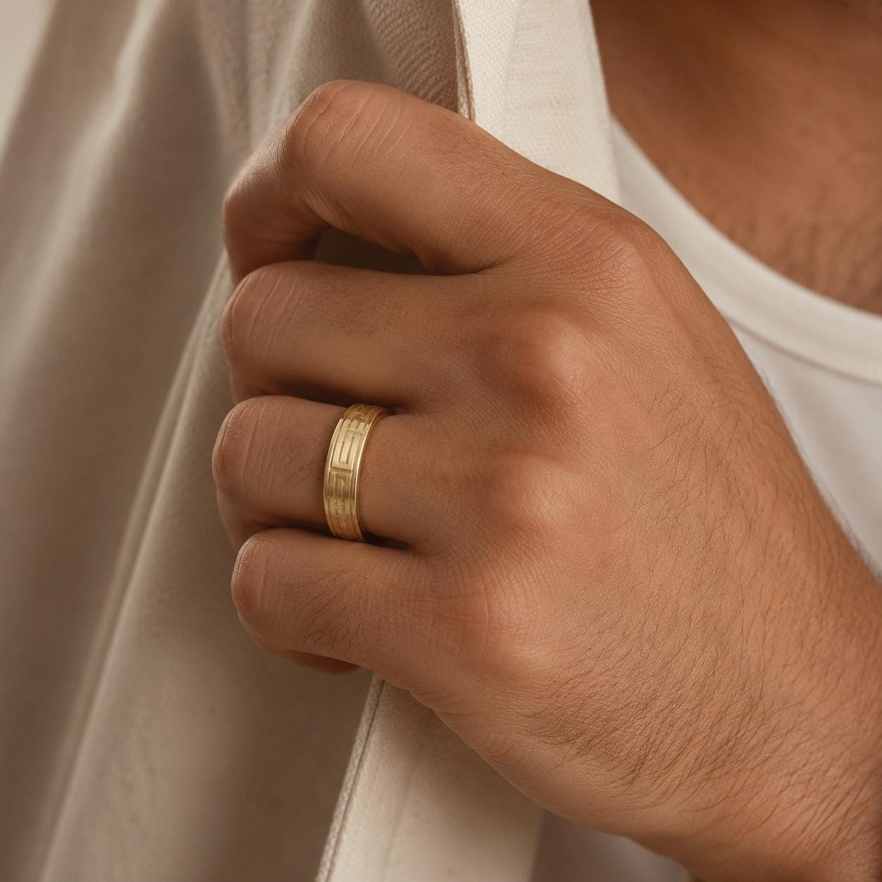 A close-up of a person's hand wearing a gold ring, with a white shirt partially visible in the background.