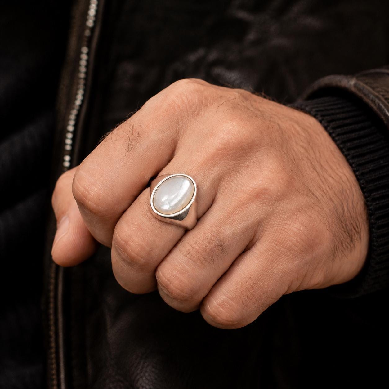 A close-up of a person's hand wearing a silver ring with a white stone.