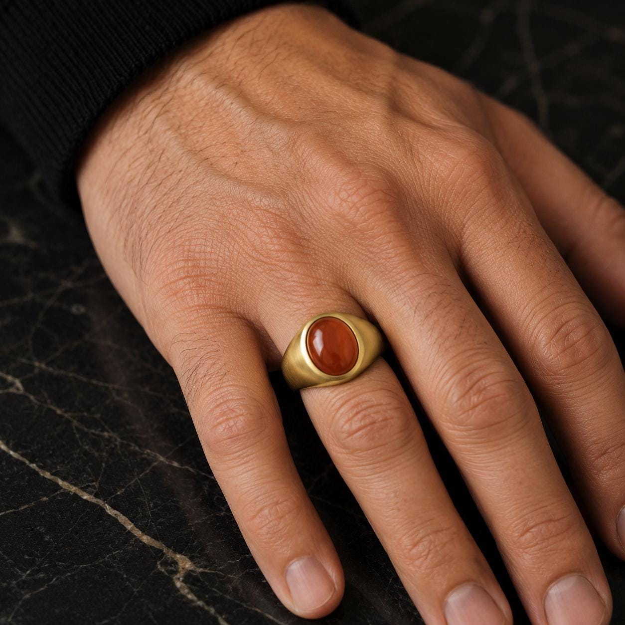 A close-up image of a person's hand wearing a gold ring with a red gemstone.