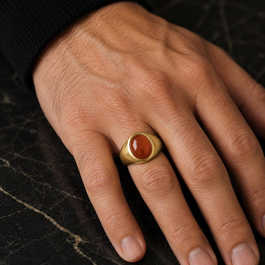 A close-up image of a person's hand wearing a gold ring with a red gemstone.
